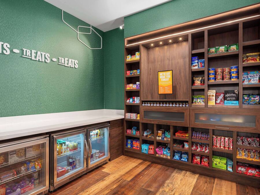 A snack bar with a green wall, wooden shelves stocked with snacks, and two glass-fronted refrigerators.