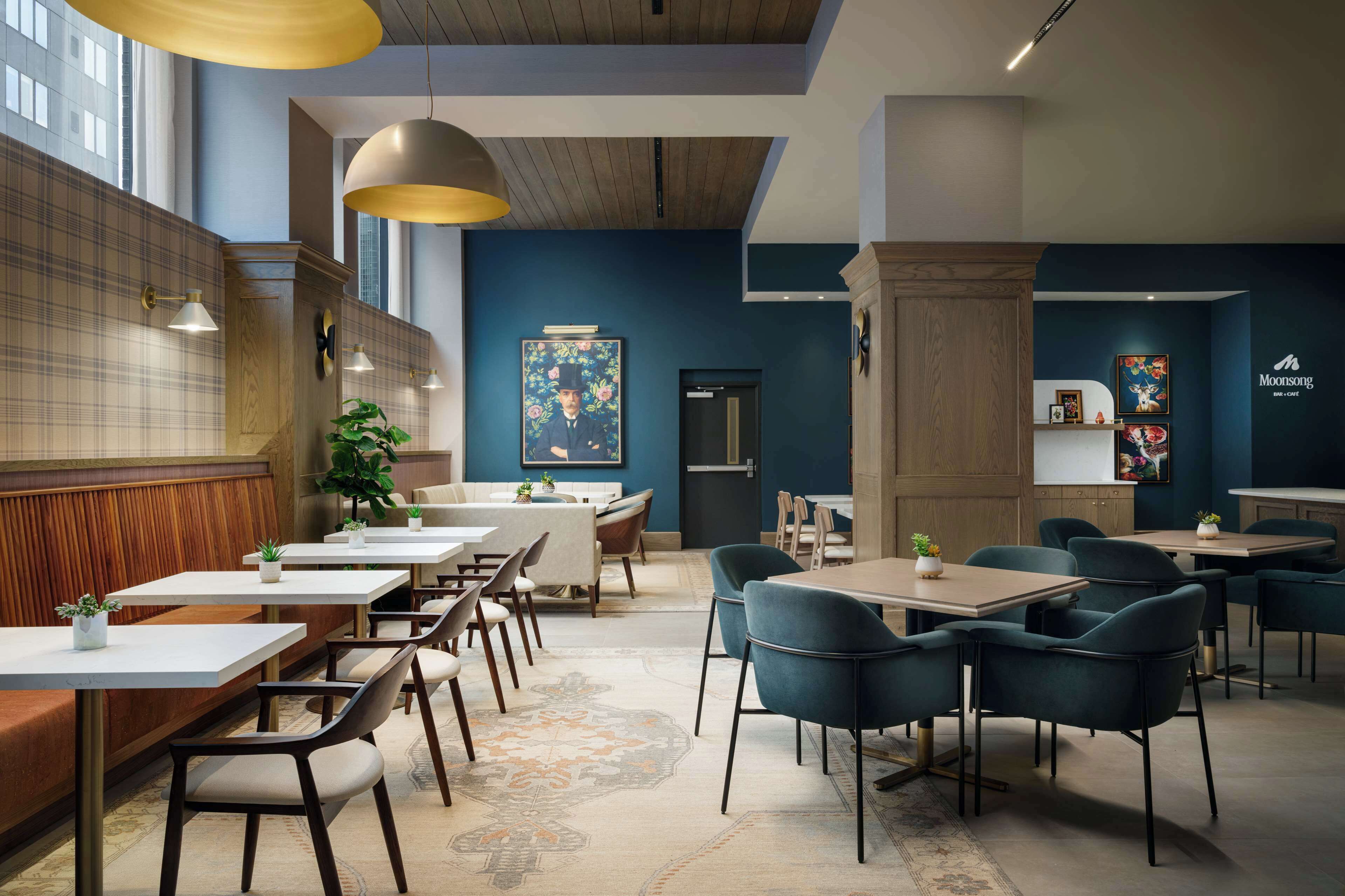 A modern restaurant interior with wooden paneling, blue walls, and a mix of white and dark blue chairs.