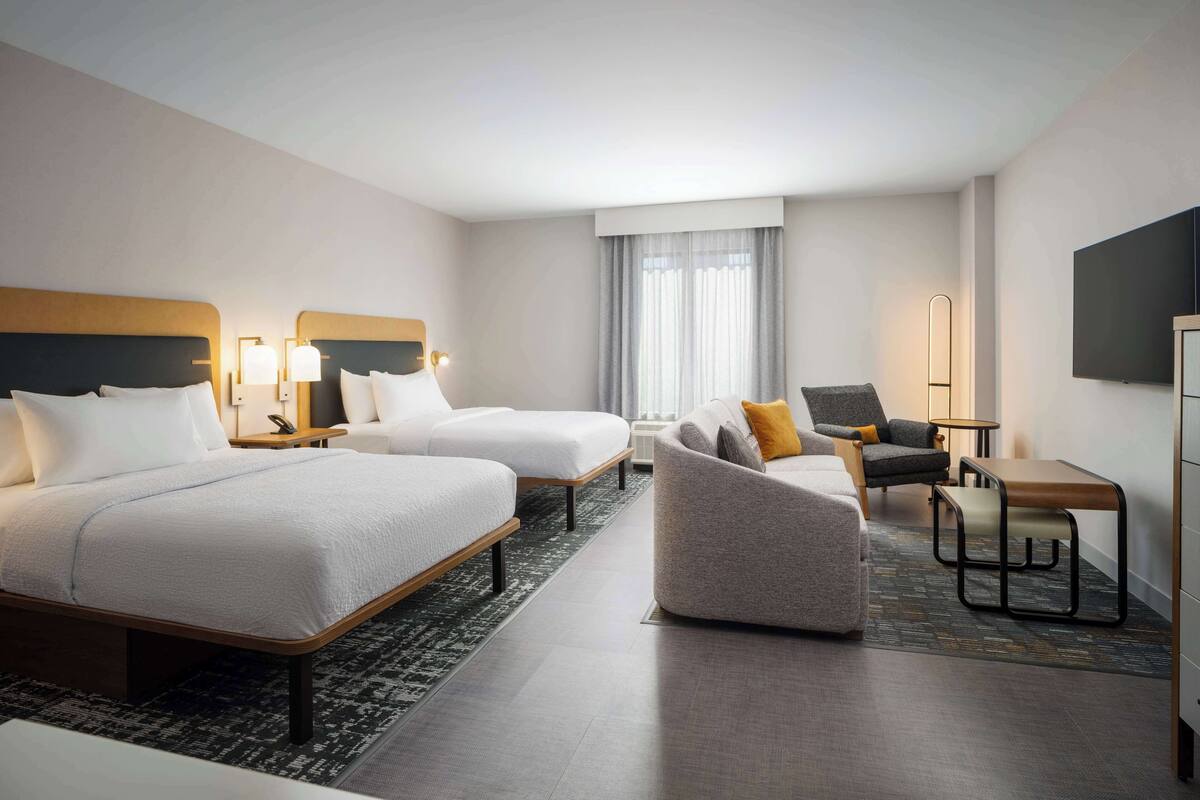 A hotel room with two beds, a sofa, a chair, a desk, and a TV.