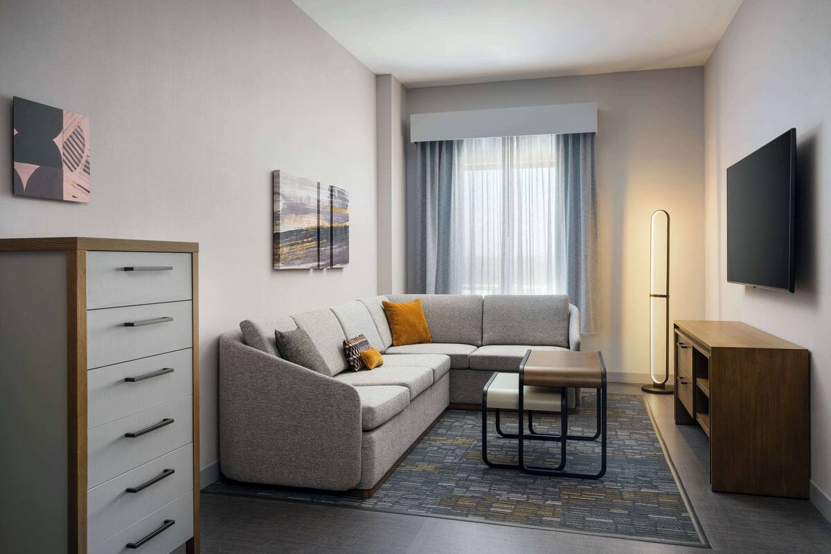 A modern living room with a sectional sofa, a small table, a cabinet, and a flat-screen TV mounted on the wall.