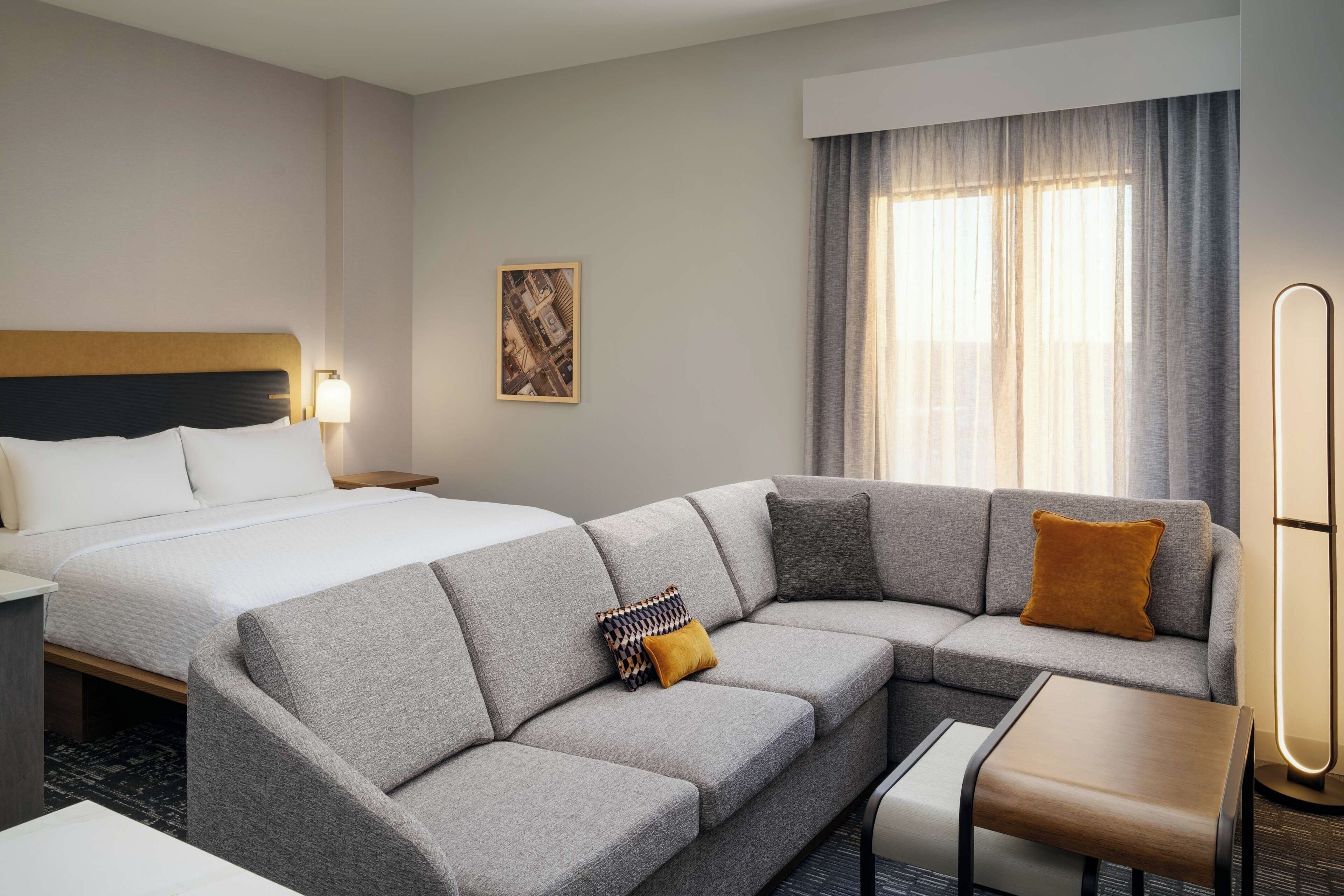 Et hotelværelse med en seng, en grå sofa, et lille bord og en gulvlampe.