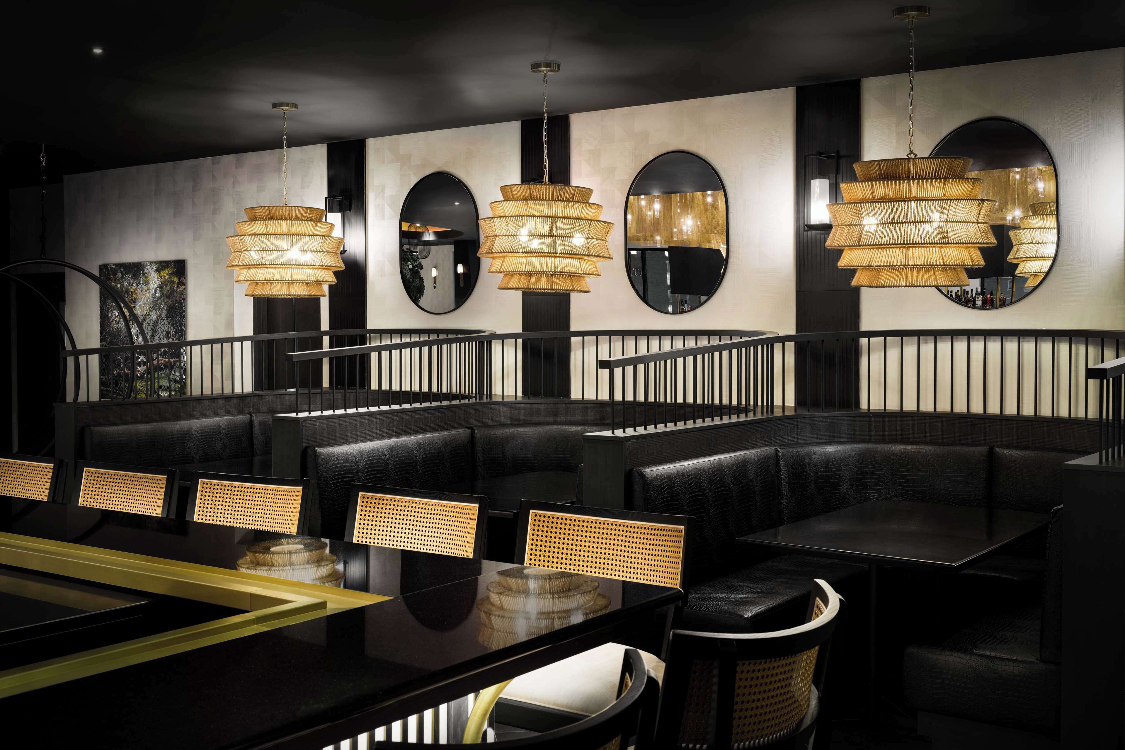 A modern restaurant with black leather booths, woven chairs, and a central black table.