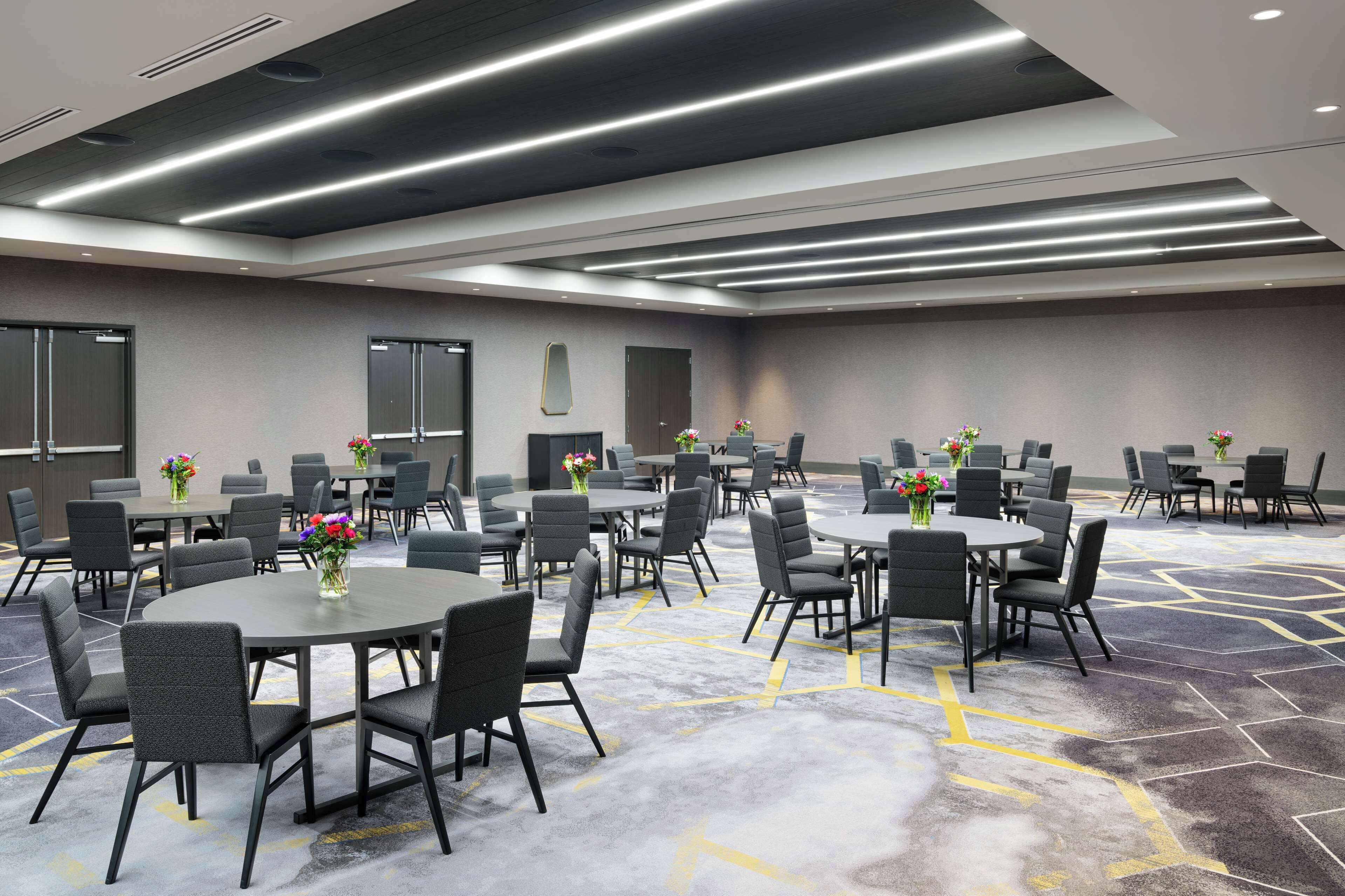 Un salón de conferencias con varias mesas y sillas, equipado con luces en el techo y suelo alfombrado.