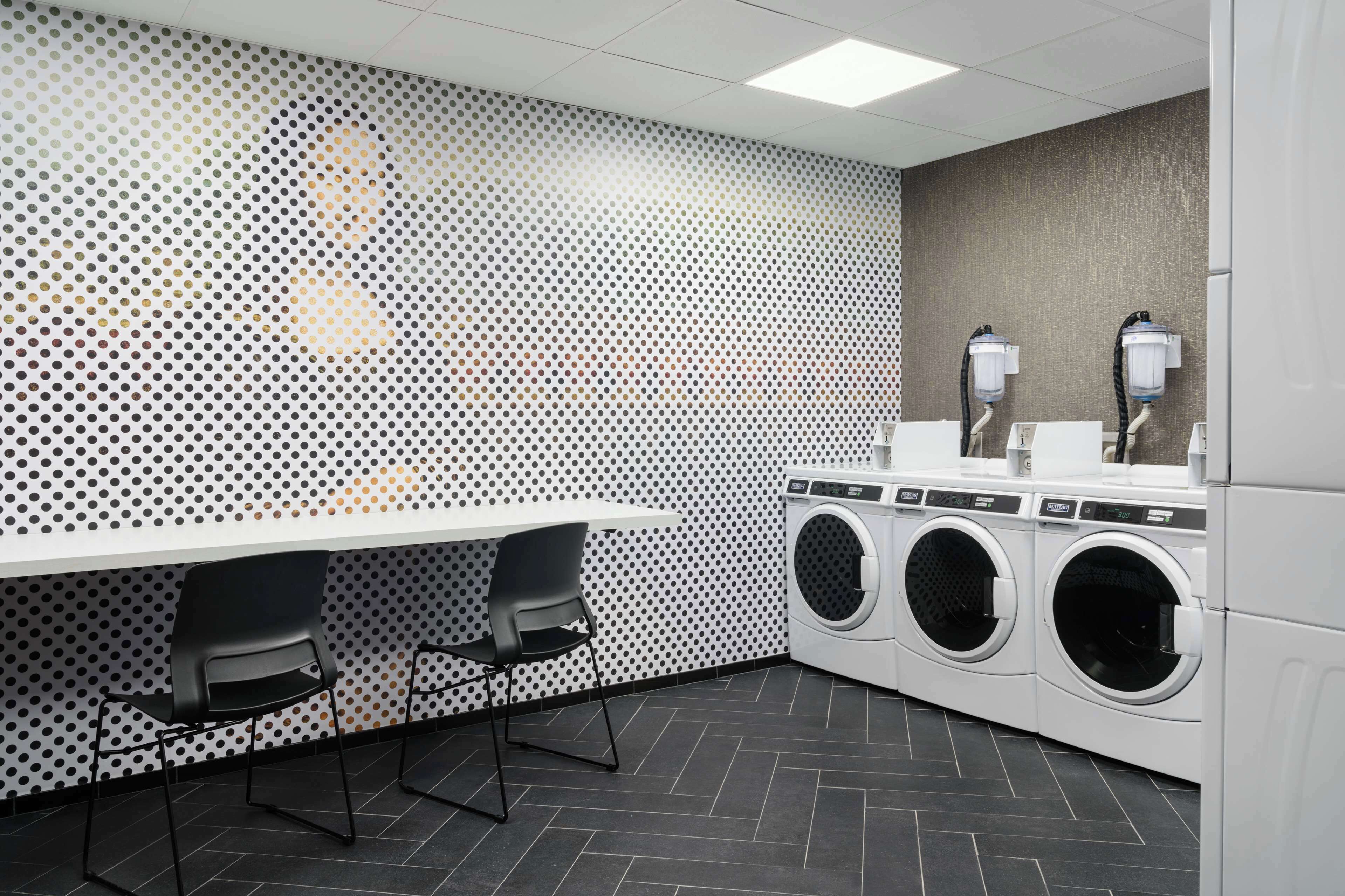 A laundry room with a perforated wall, two chairs, and a row of washing machines.