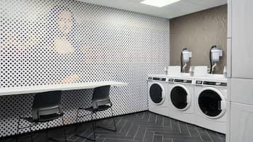 A laundry room with a perforated wall, two chairs, and a row of washing machines.