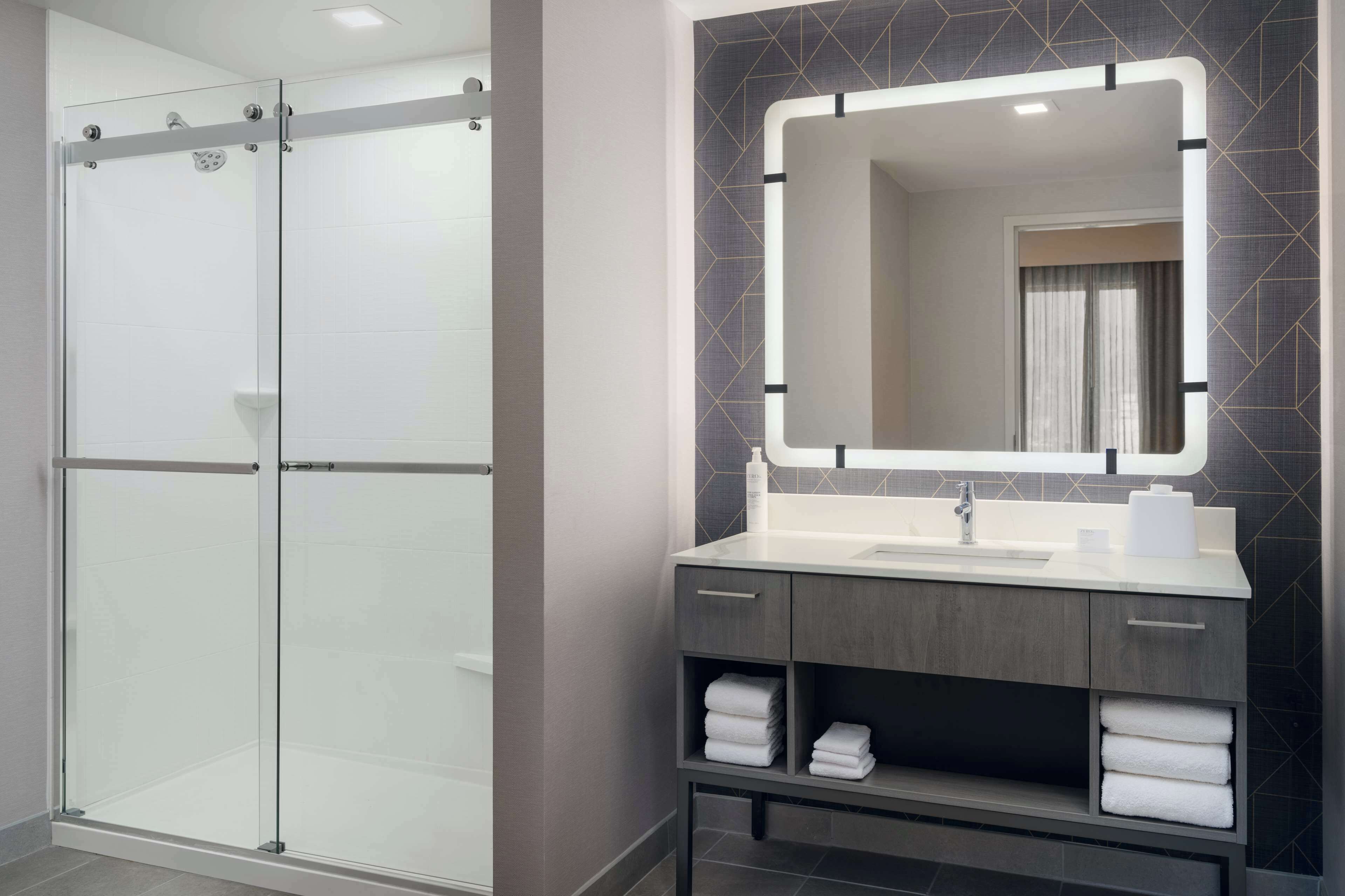 A modern bathroom with a glass shower enclosure, a vanity with a mirror, and neatly arranged towels.