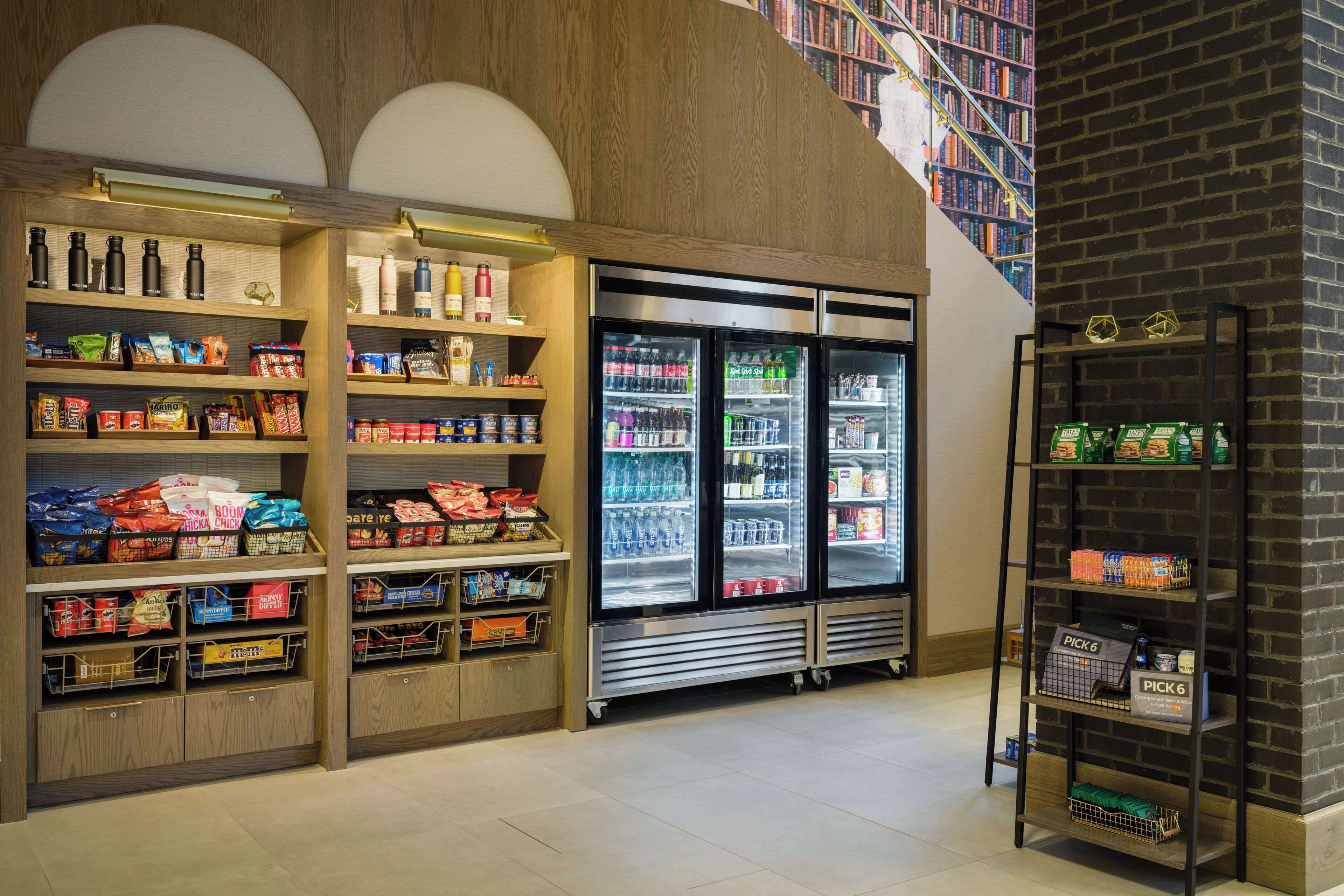 A grocery store with shelves stocked with snacks and beverages, a refrigerated display, and a ladder shelf.