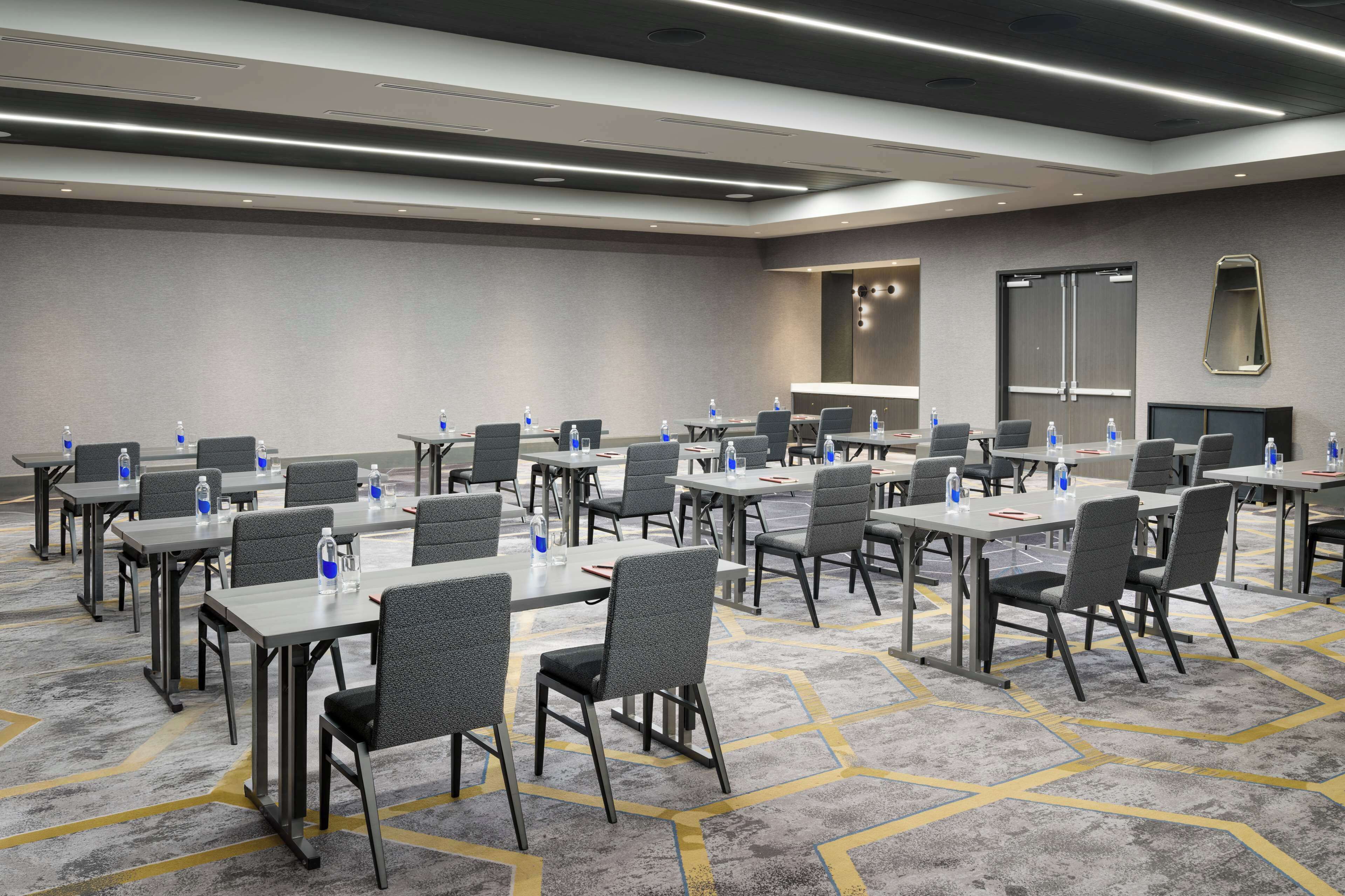 A conference room with multiple tables and chairs, equipped with water bottles and red folders.
