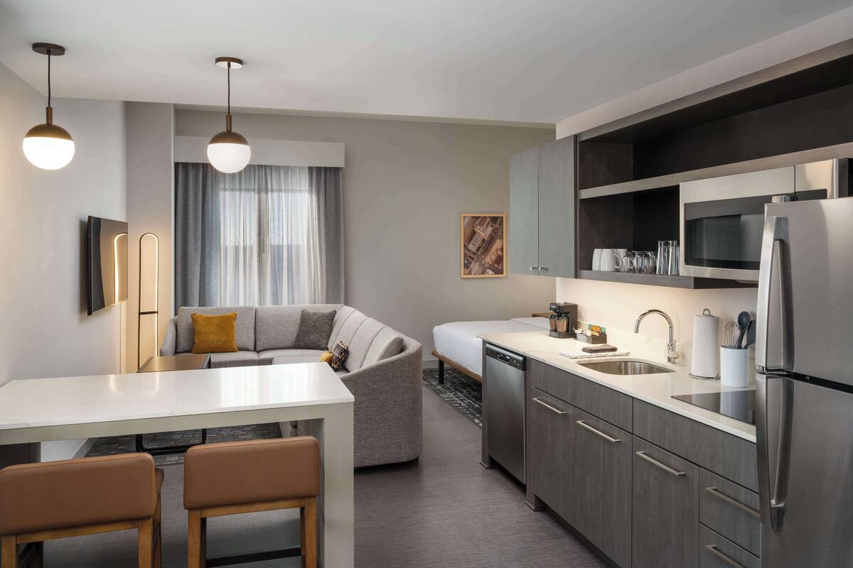 A modern kitchen with a dining area, stainless steel appliances, and a gray sofa.