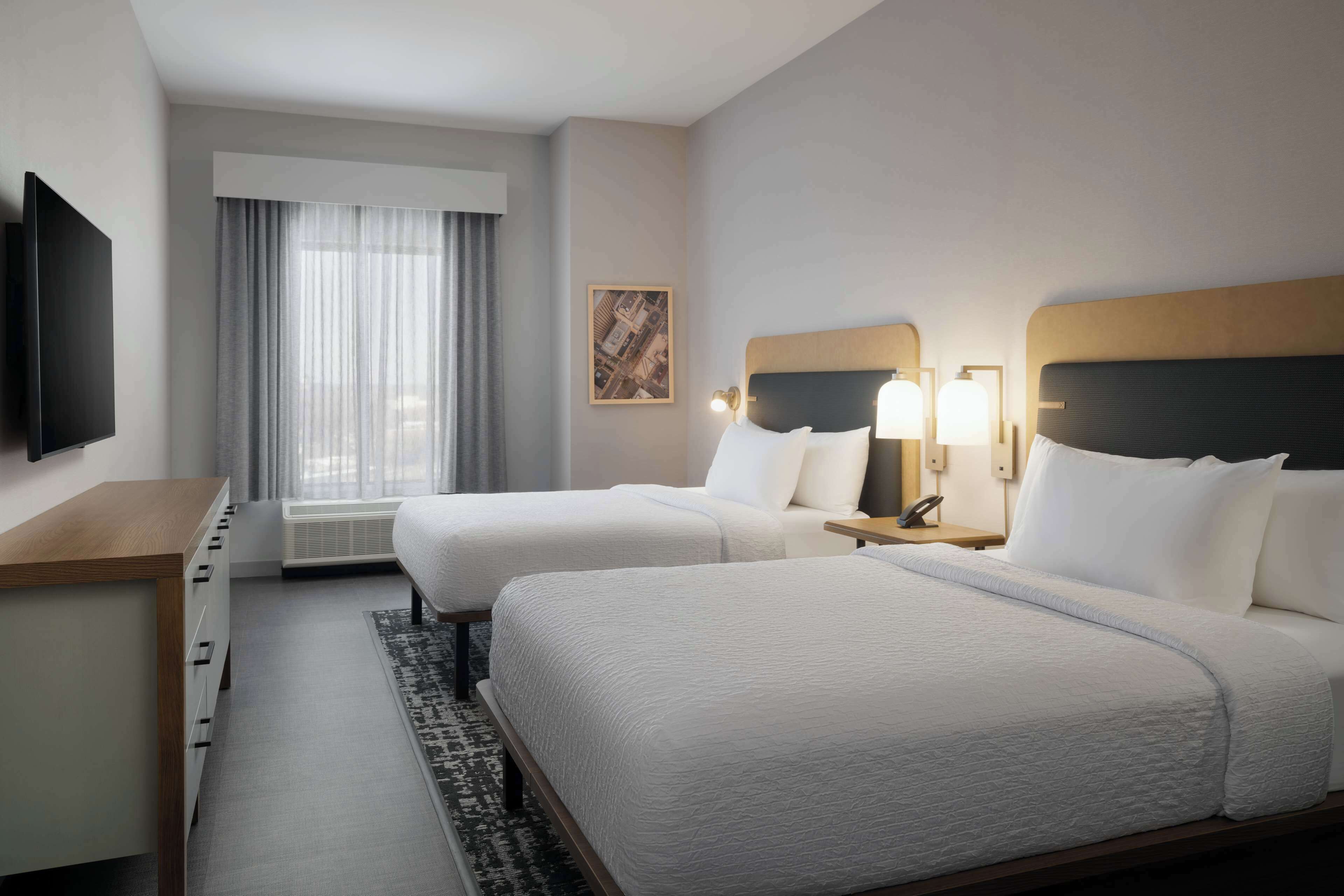 A hotel room with two beds, a desk, a TV, and a window with curtains.