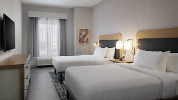 A hotel room with two beds, a desk, a TV, and a window with curtains.