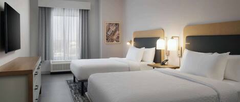 A hotel room with two beds, a desk, a TV, and a window with curtains.