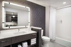 A modern bathroom with a large mirror, a white sink, dark patterned wall, and a shower area. - Homewood Suites by Hilton Raleigh Downtown (Raleigh)