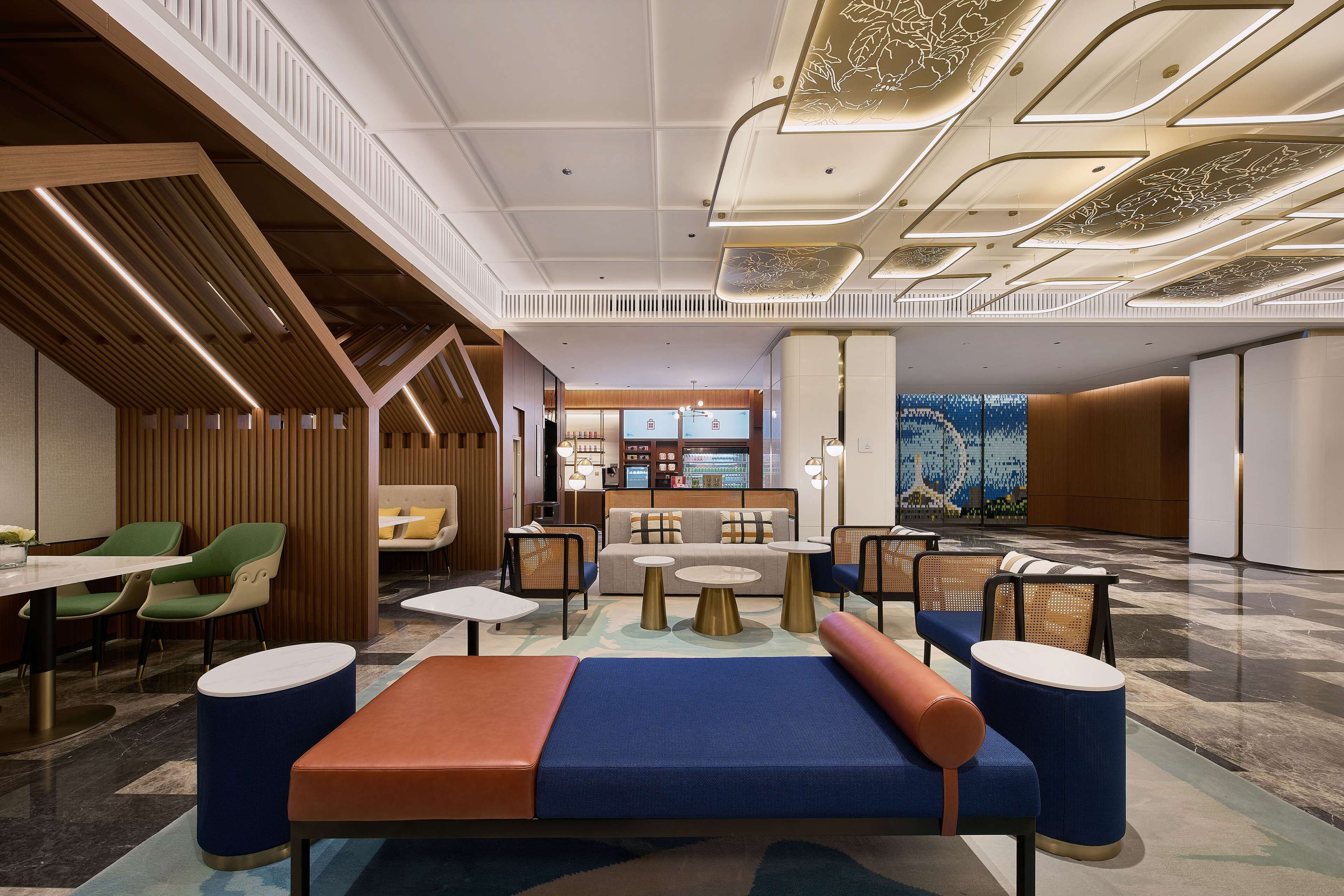 A modern hotel lobby with seating areas, a reception desk, and a view of the restaurant in the background.