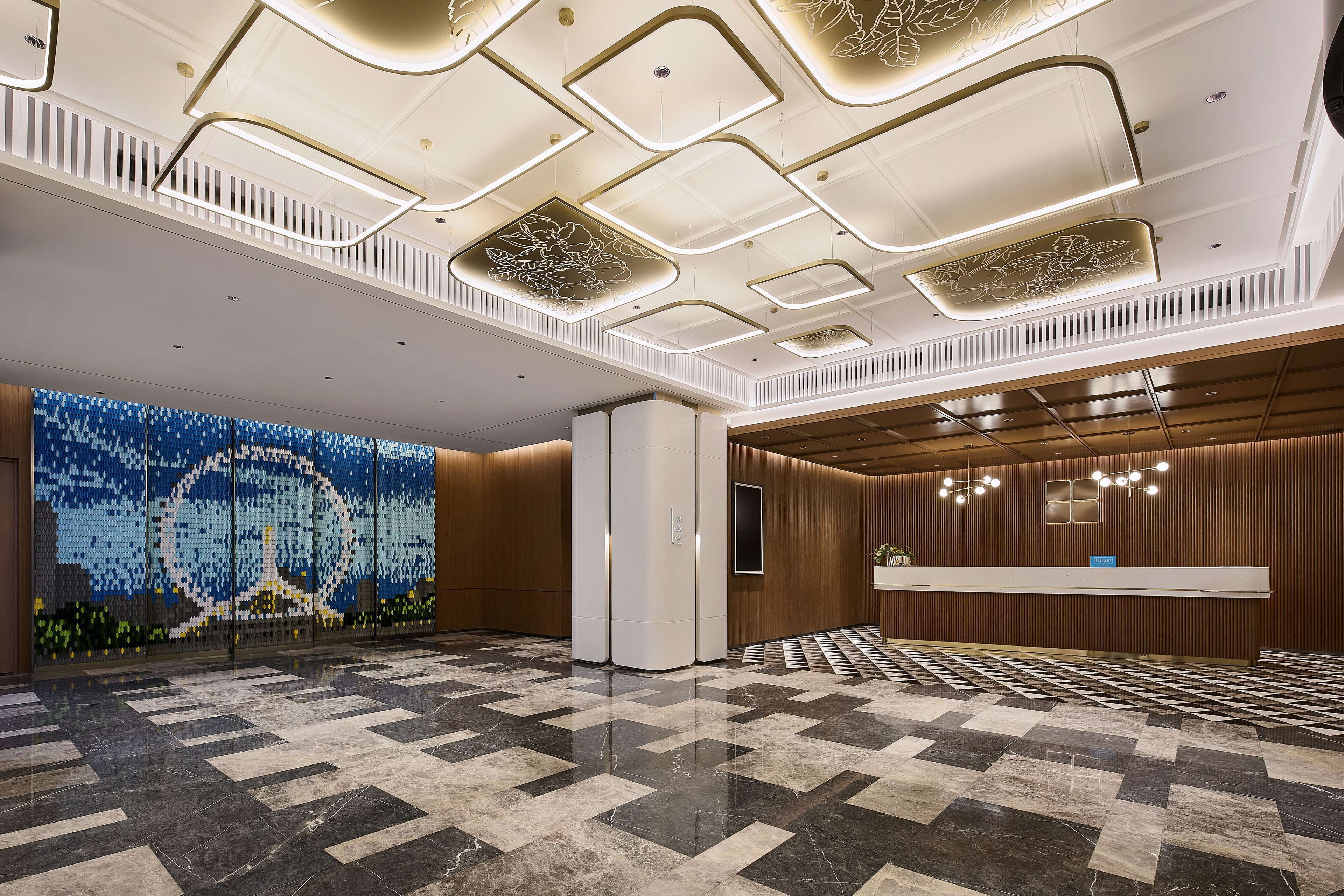A spacious lobby with a checkered floor, a reception desk, and a decorative wall with a mosaic design.