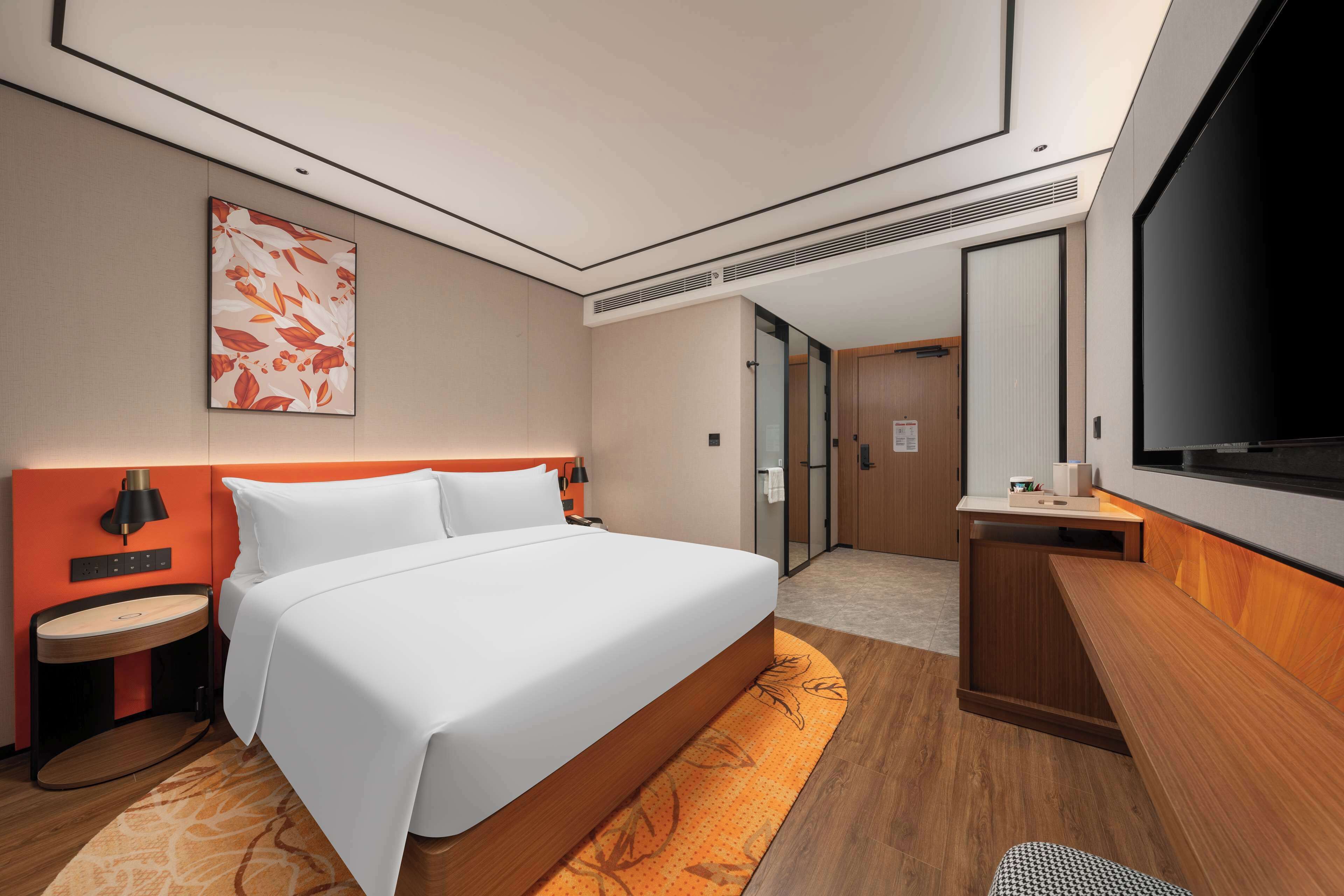 Een moderne hotelkamer met een groot bed, een bureau, een televisie en een badkamer zichtbaar door een geopende deur.
