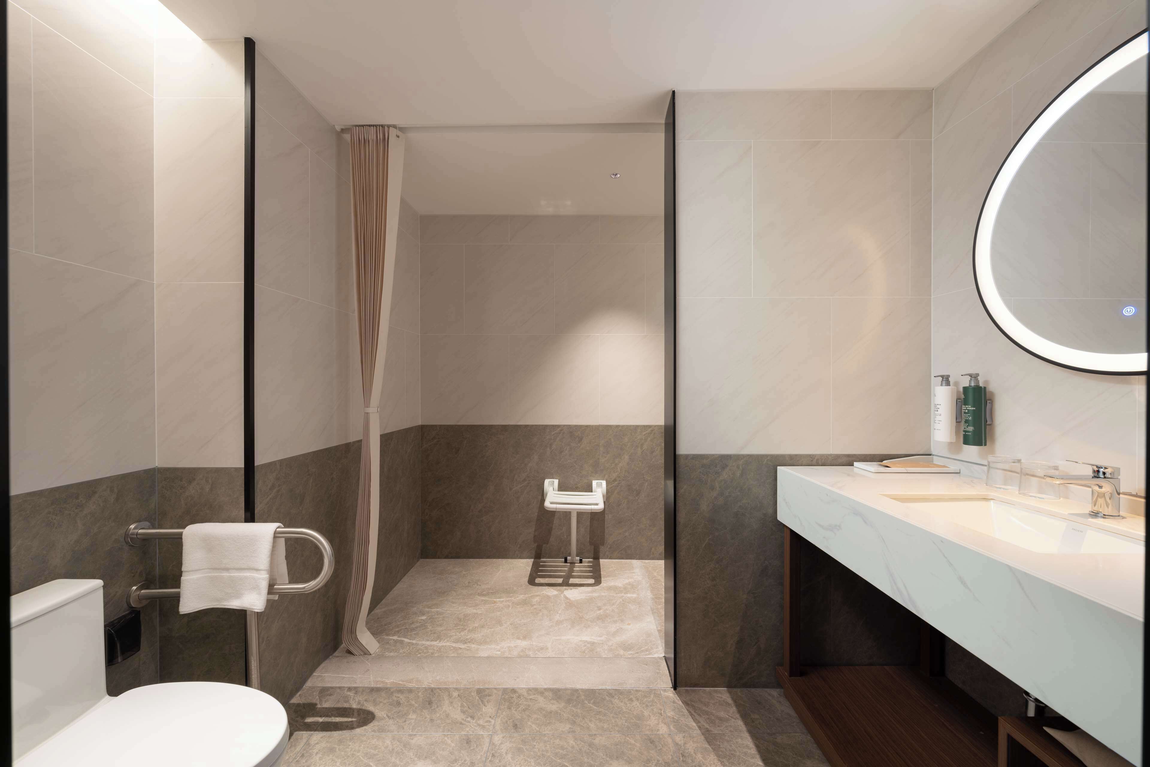 Ein modernes Badezimmer mit Toilette, einer Duschkabine, einem Waschbecken mit Spiegel und einem Handtuchhalter.