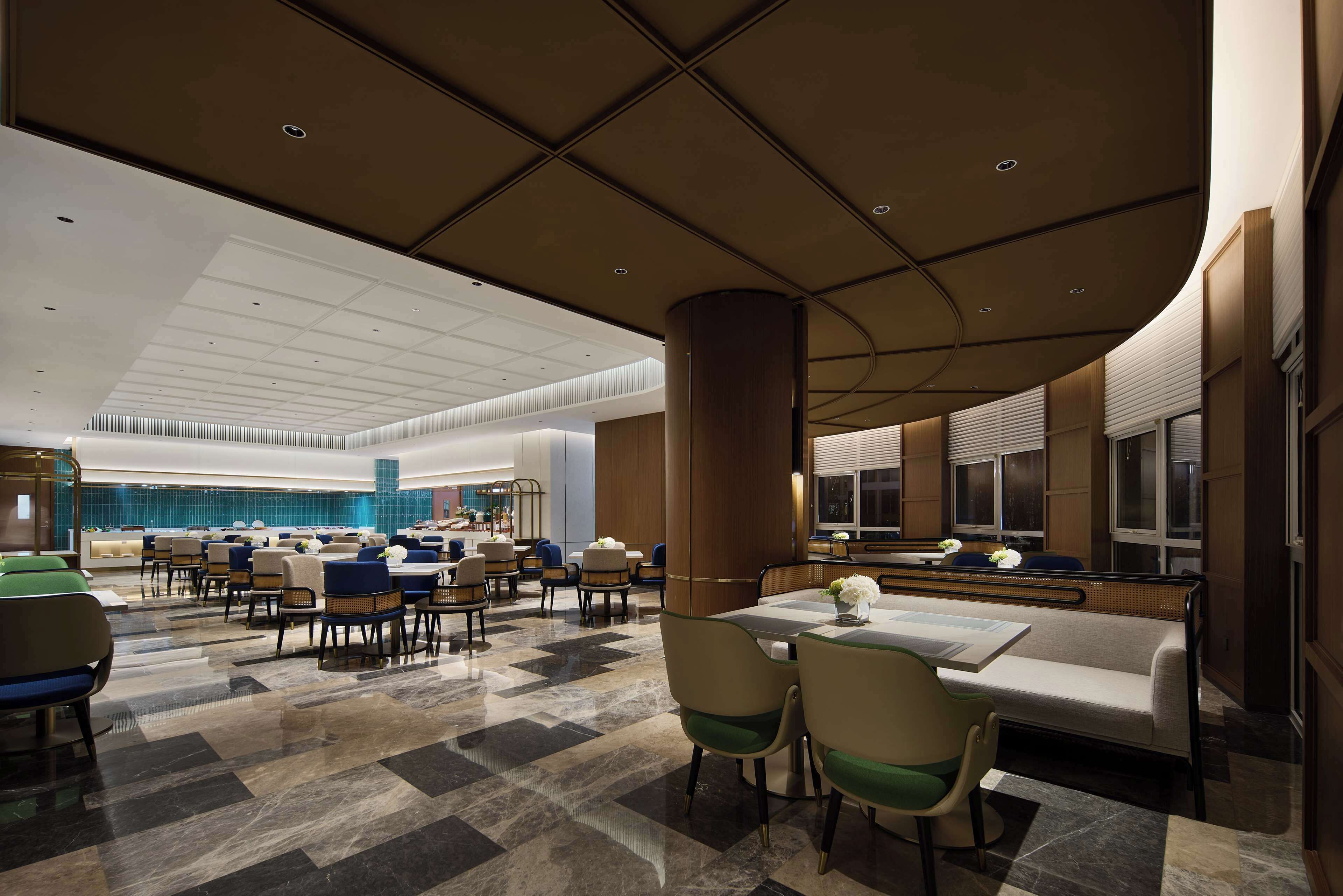 A spacious hotel lobby with a checkered floor, multiple seating areas, and a large reception desk.