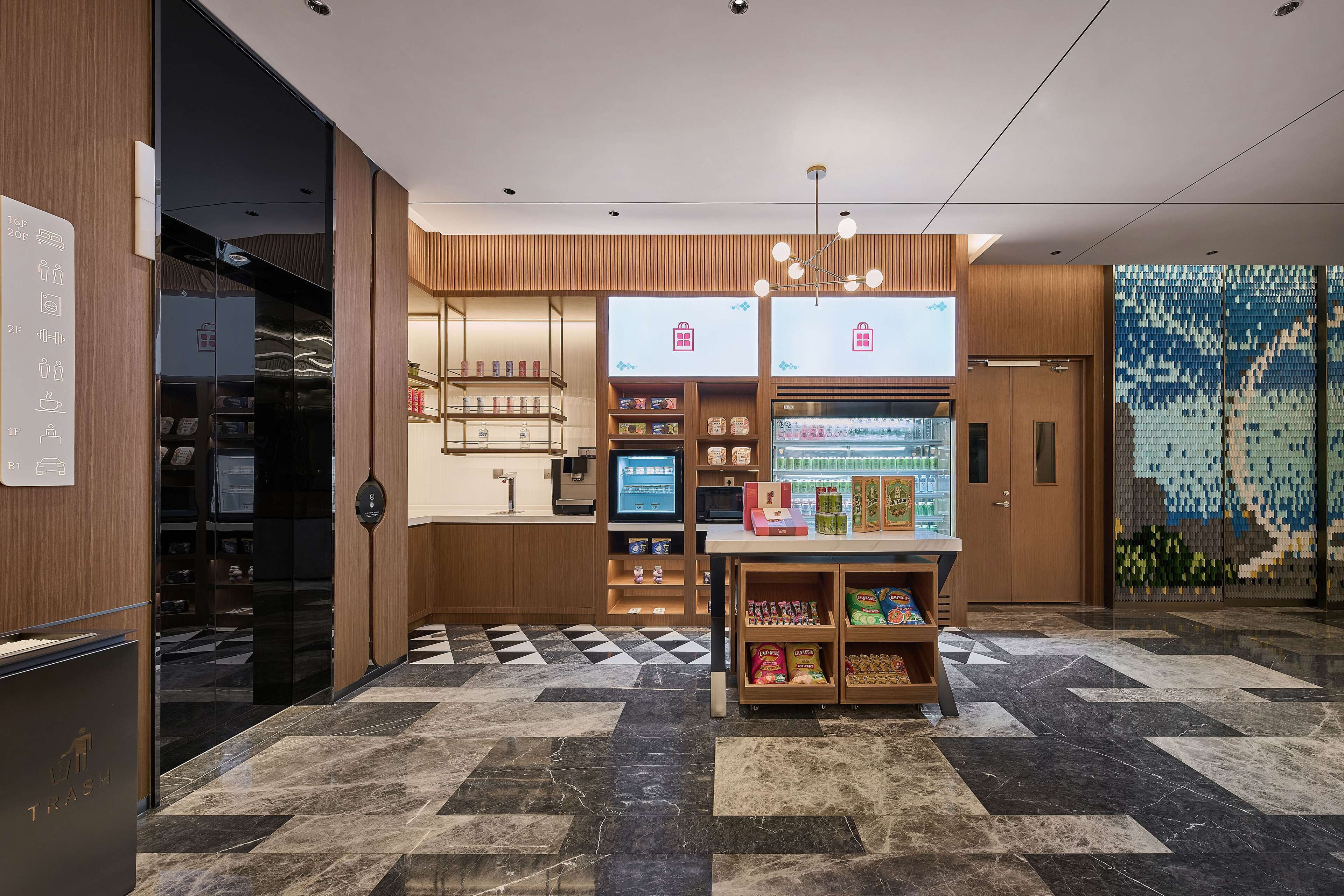 Un moderno vestíbulo de hotel con mostrador de recepción, pantalla digital y barra de aperitivos.