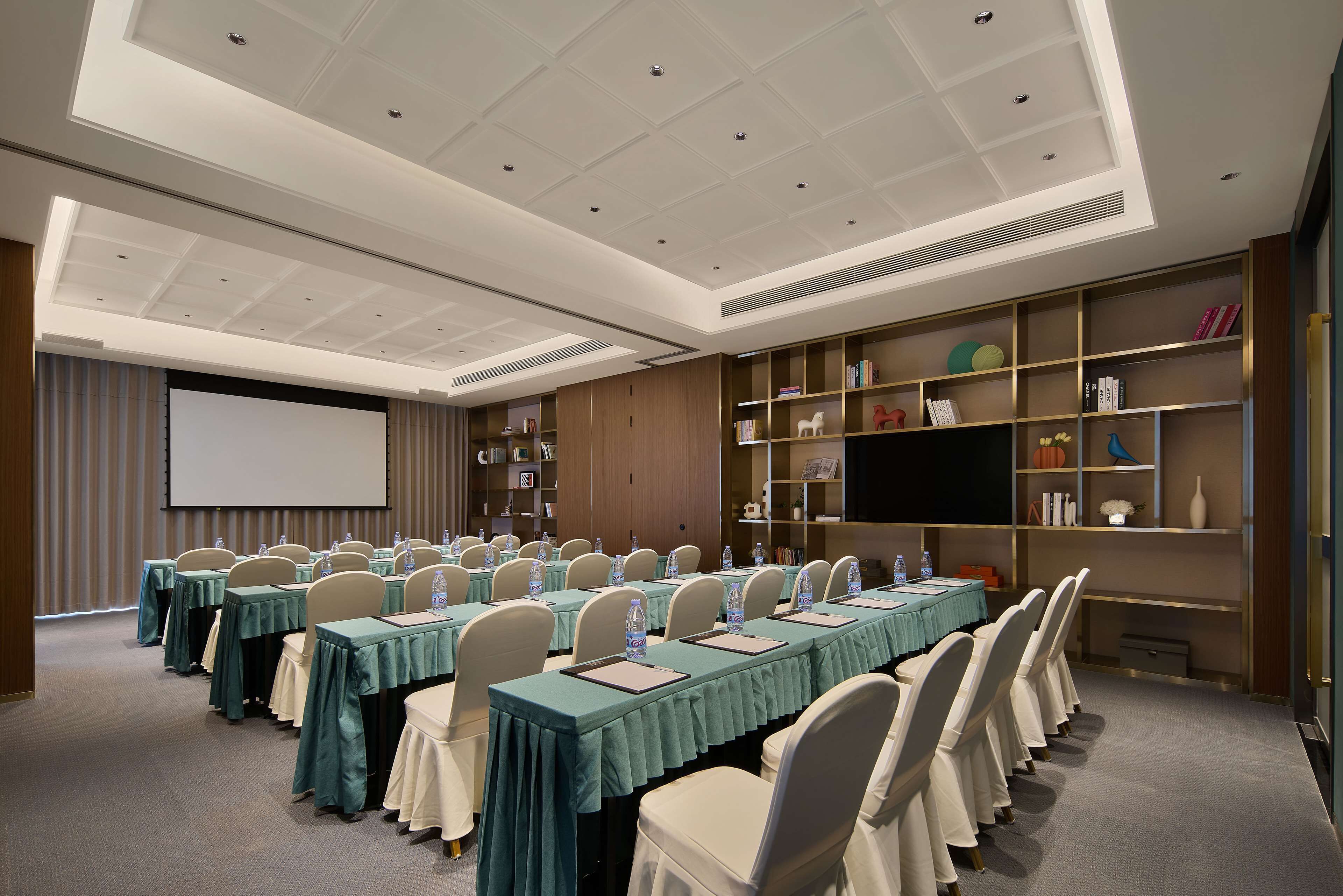 Une salle de conférence équipée de longues tables, de chaises et d’un écran de projection.