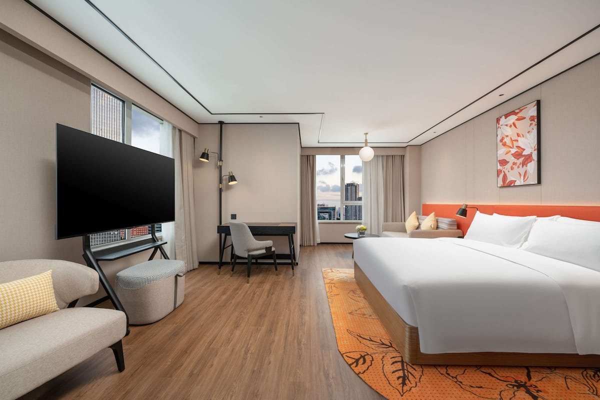 Ein Hotelzimmer mit Bett, Schreibtisch, Fernseher und Blick auf die Stadt.
