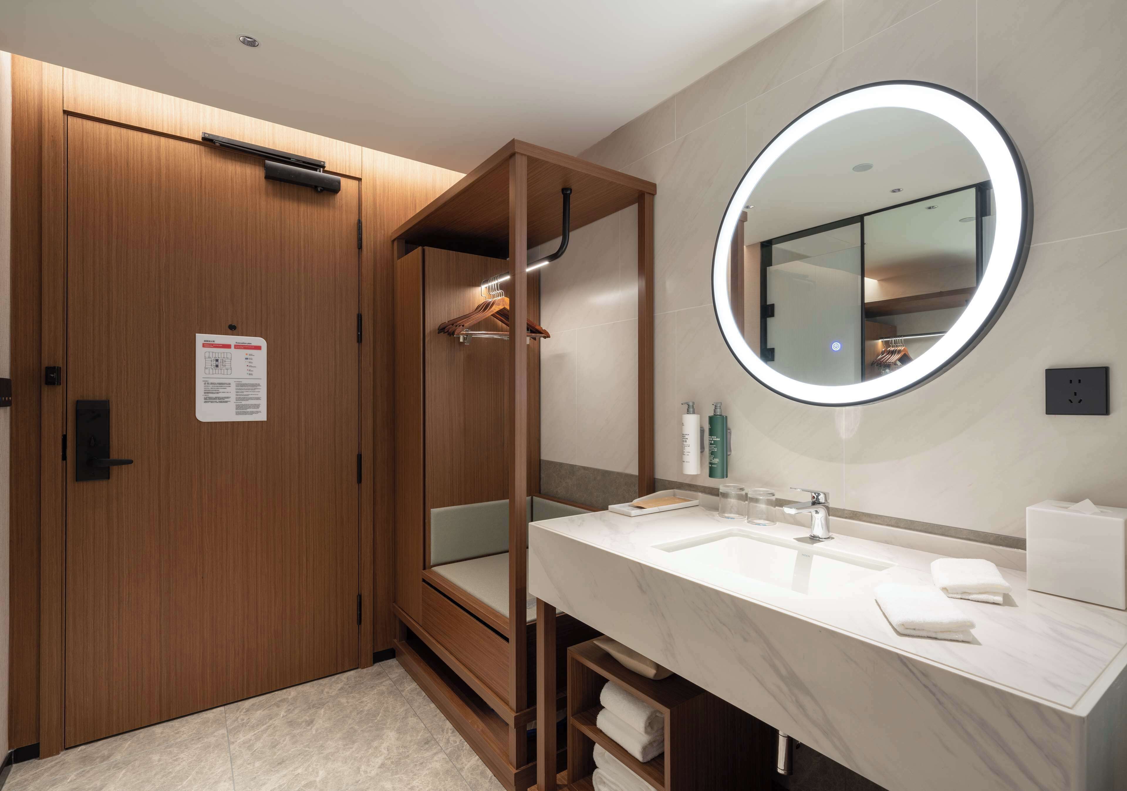 A modern bathroom with a wooden vanity, a round mirror, and a built-in shower.