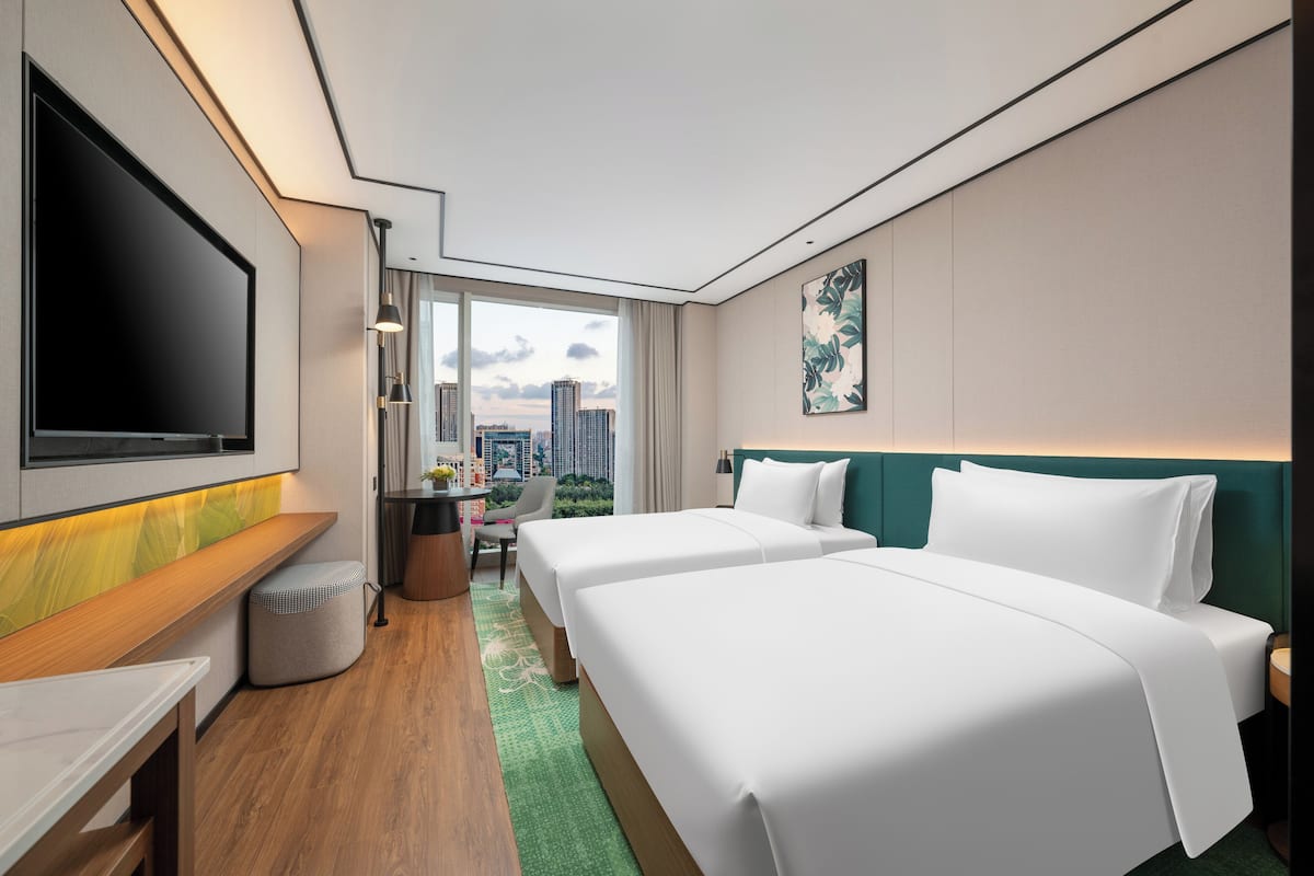 Ein Hotelzimmer mit zwei Betten, einem Fernseher, einem Schreibtisch und Blick auf die Stadt.