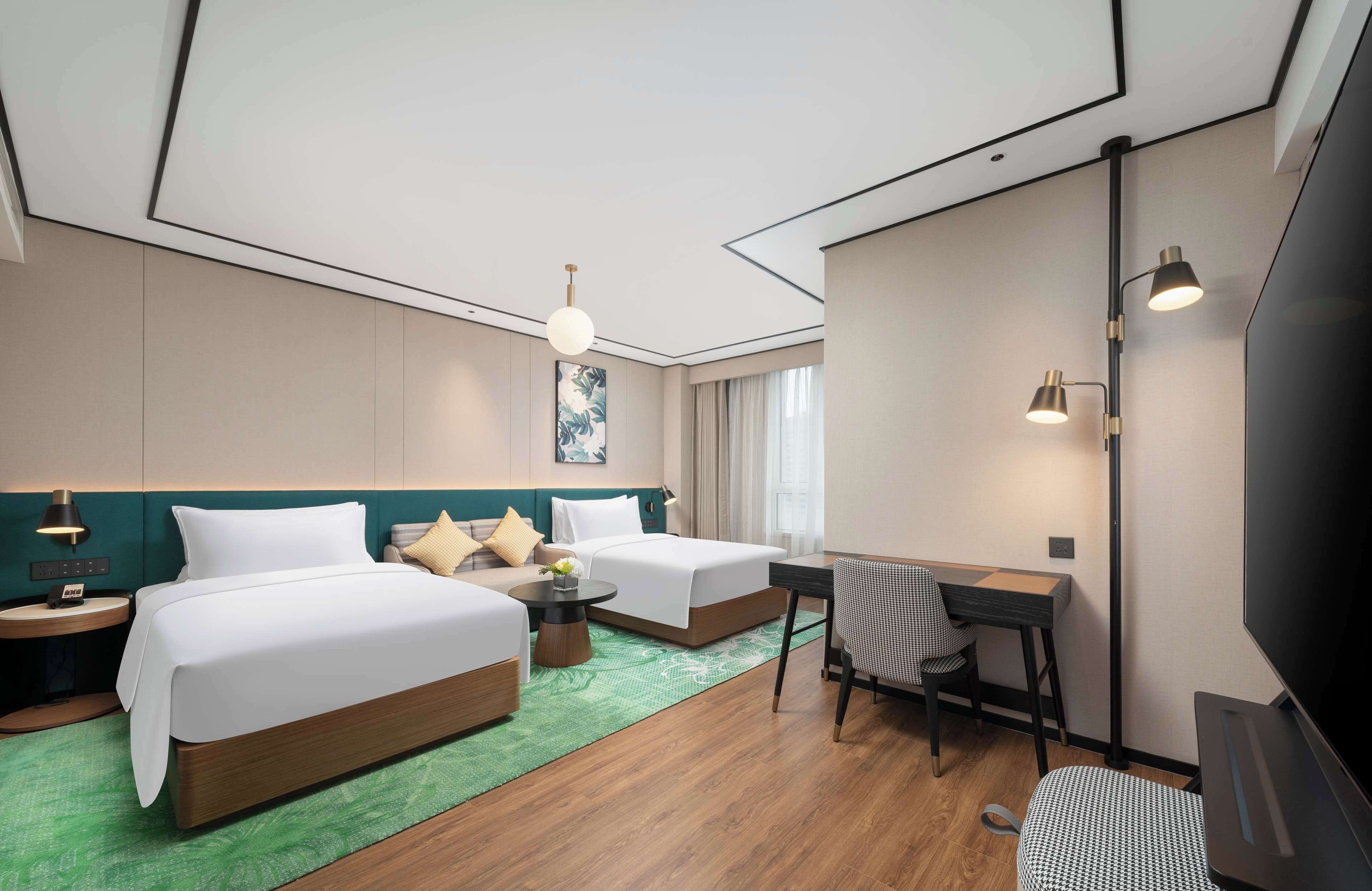 Habitación de hotel con dos camas, un escritorio, una silla, un televisor y una alfombra verde.