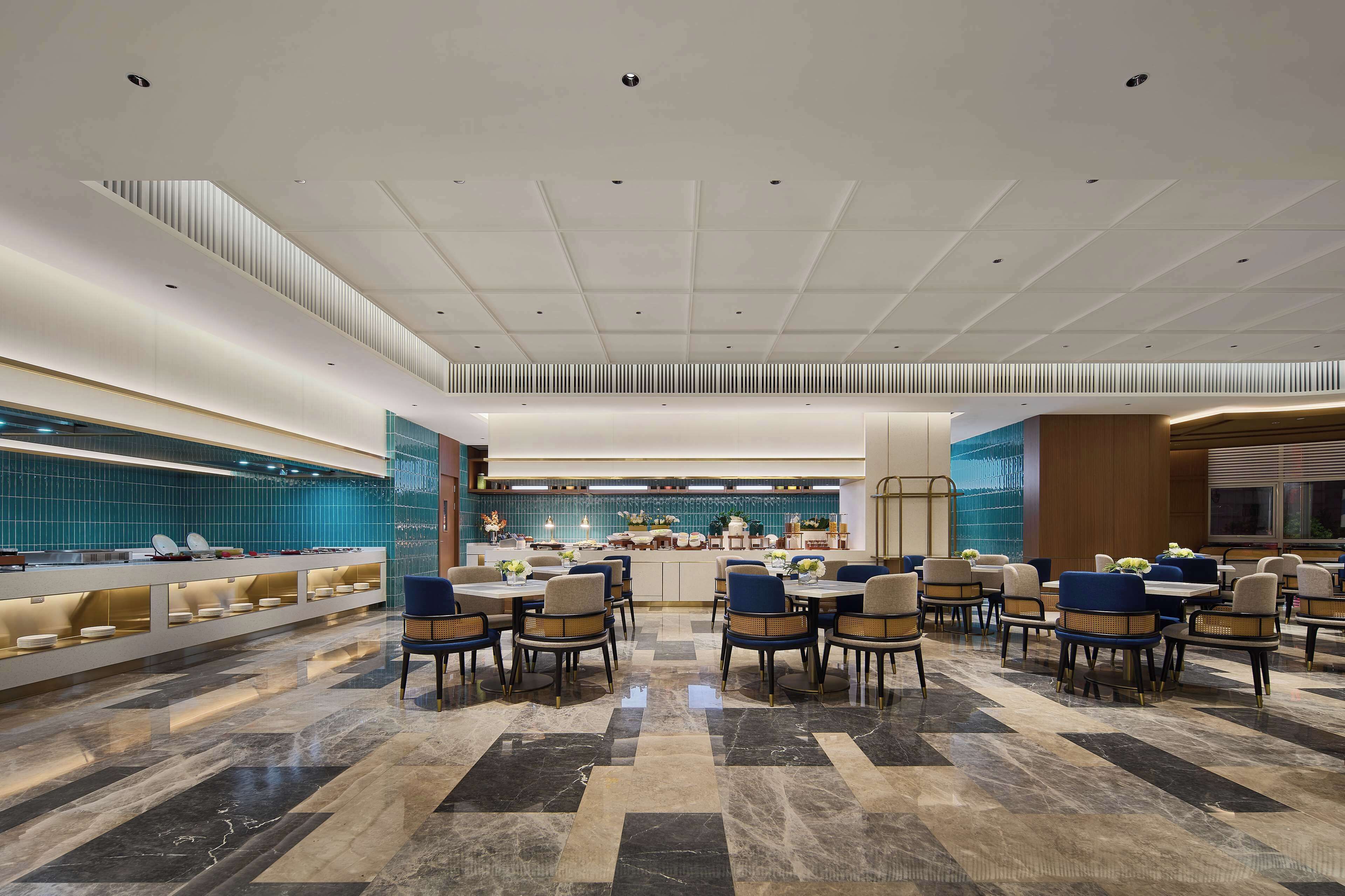 A modern hotel lobby with a long reception desk, multiple seating areas, and a tiled backsplash.