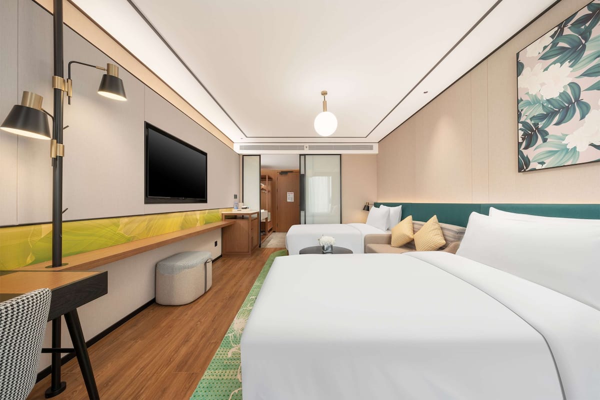 Ein modernes Hotelzimmer mit einem Bett, einem Schreibtisch, einem Fernseher und einem durch eine Glastür einsehbaren Badezimmer.