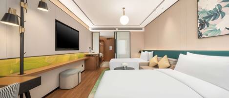 A modern hotel room with a bed, a desk, a TV, and a bathroom visible through a glass door.
