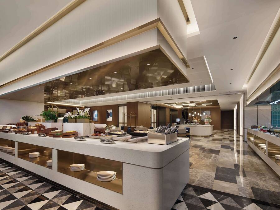 Um hall de hotel moderno com um balcão de recepção central, uma grande janela de vidro e um balcão de check-in.