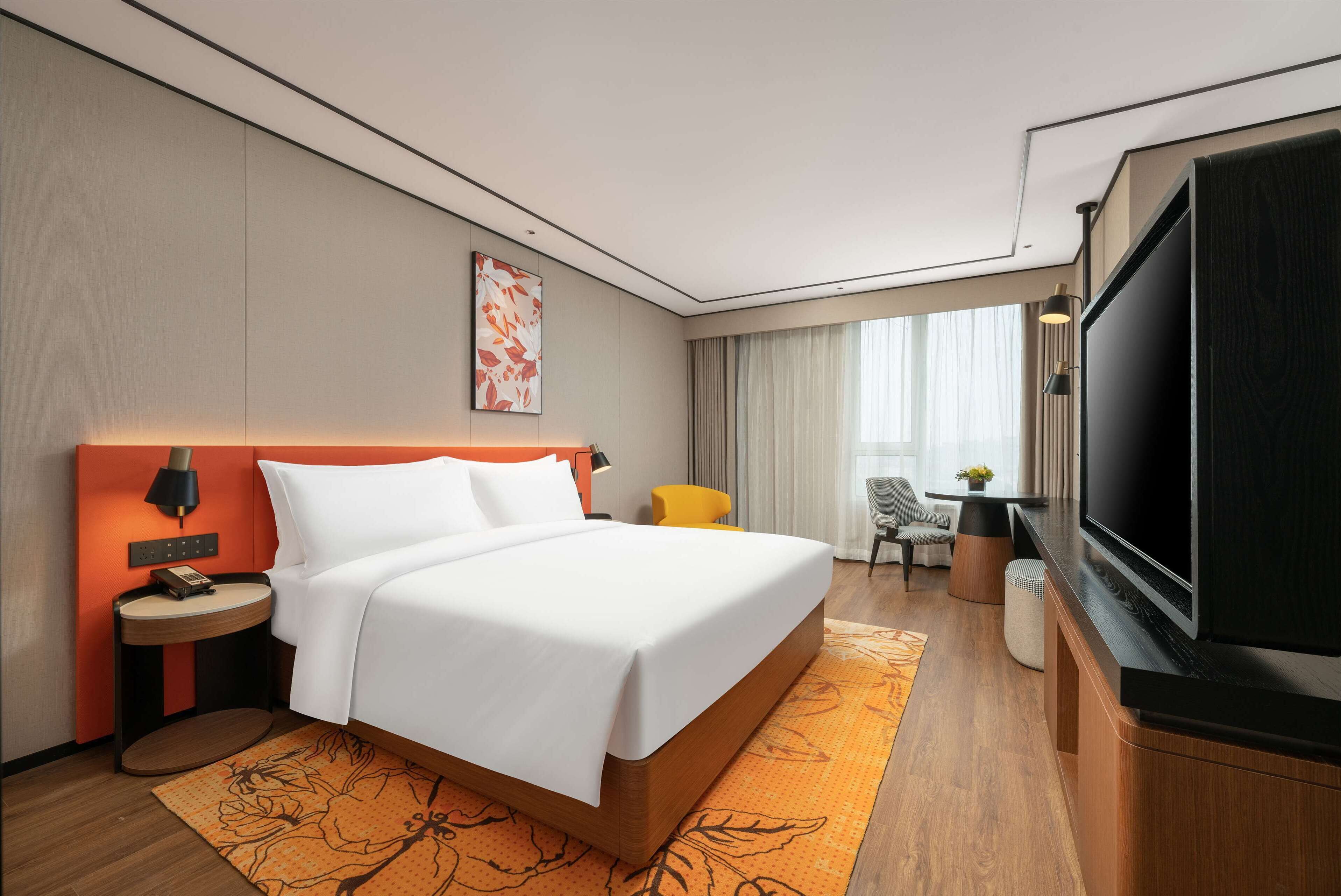 A hotel room with a large bed, a flat-screen TV, a desk with a chair, and a window with curtains.
