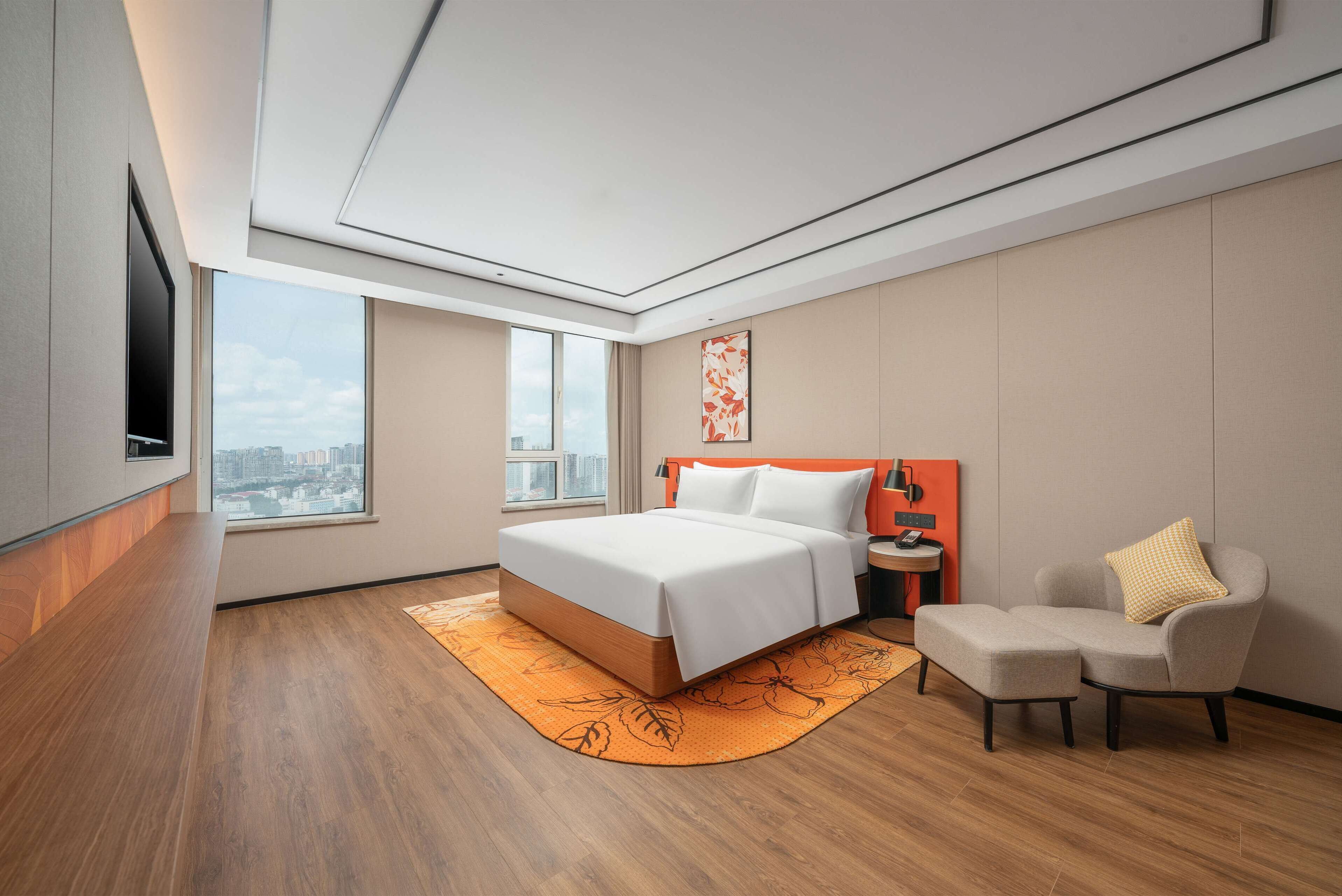 A modern hotel room with a large bed, a seating area, and a city view.