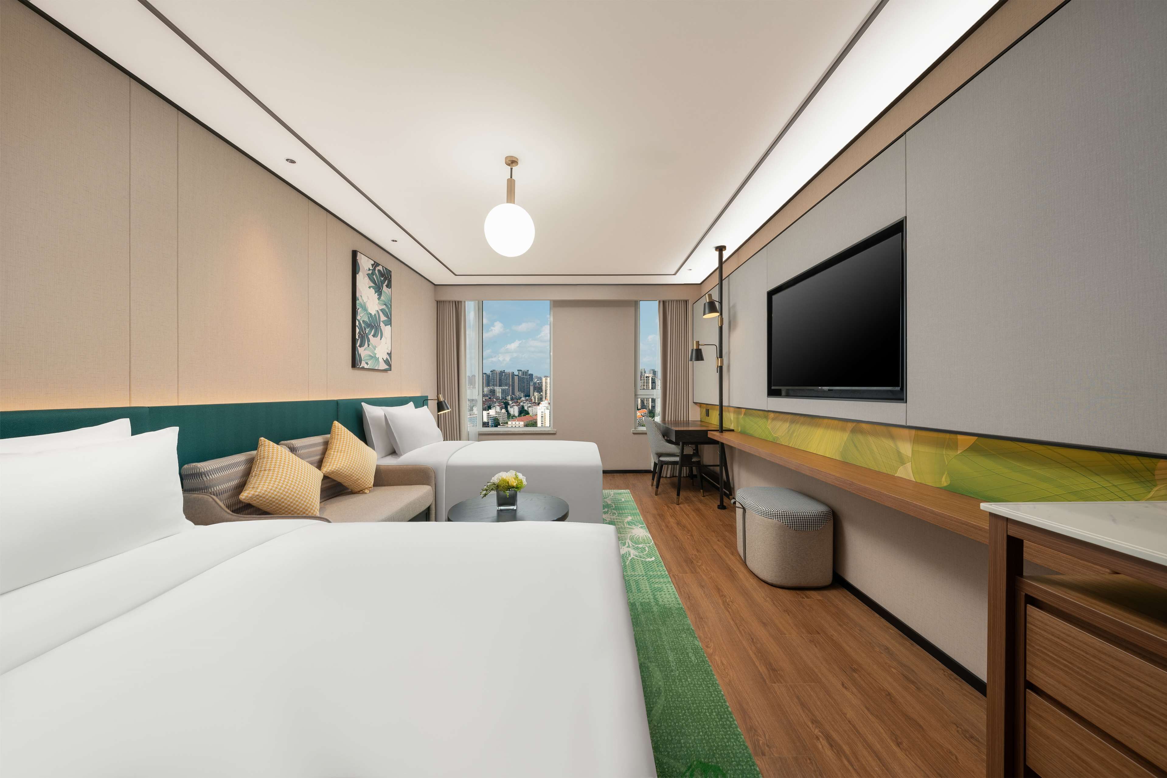 A modern hotel room with two beds, a desk, a TV, and a view of the city skyline.