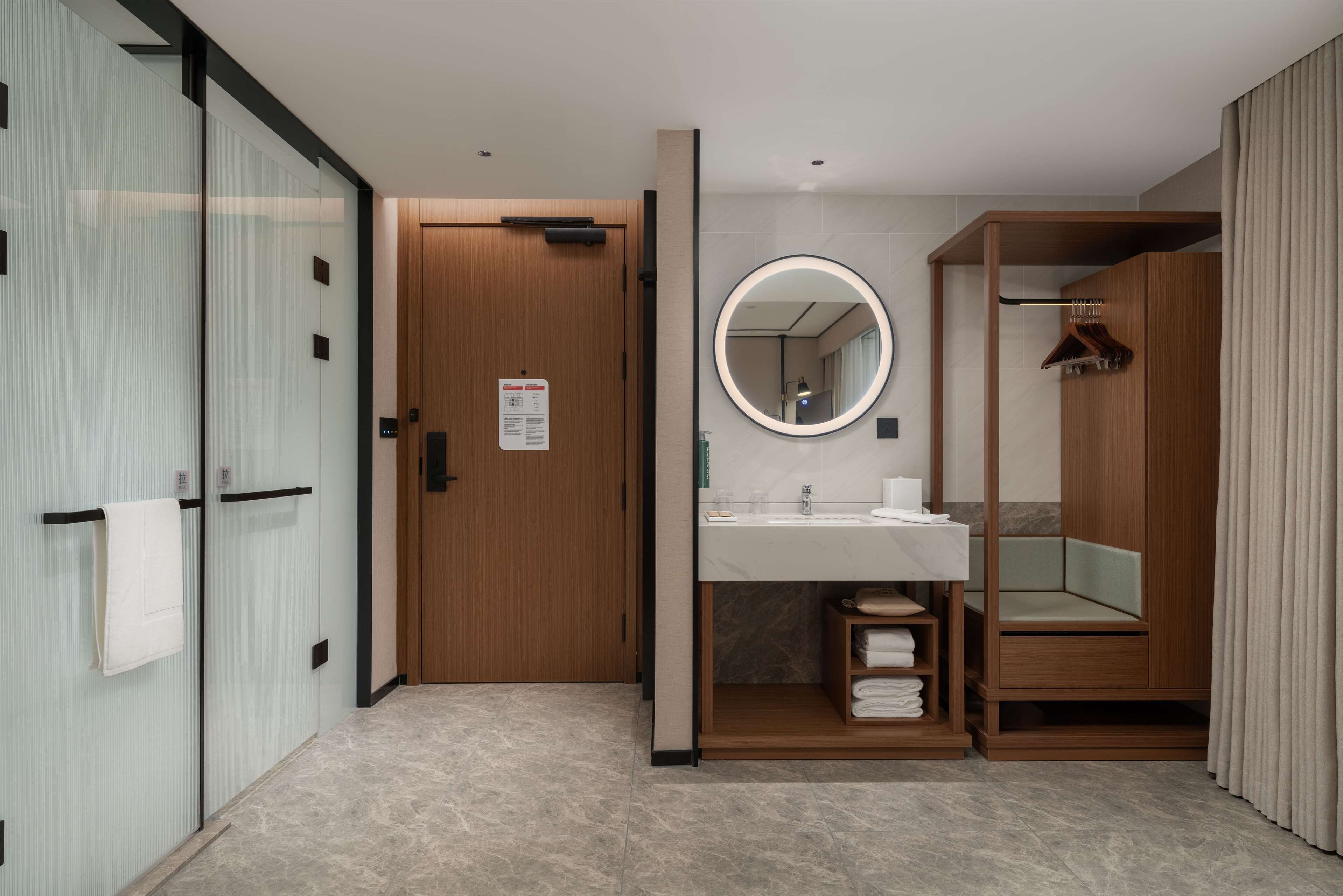 A modern bathroom with a glass partition, wooden door, and a vanity with a mirror.