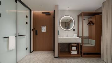 A modern bathroom with a glass partition, wooden door, and a vanity with a mirror.