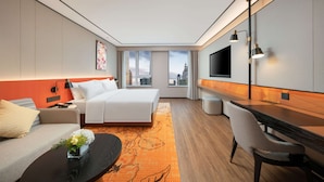 Une chambre d’hôtel moderne équipée d’un lit, d’un canapé, d’un bureau et d’une grande fenêtre donnant sur la ville.