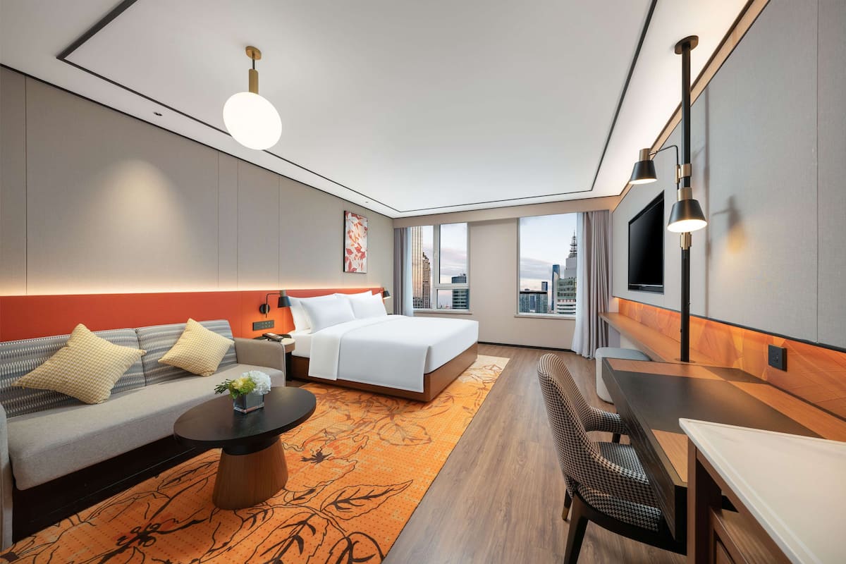 Ein modernes Hotelzimmer mit Bett, Sofa, Esstisch und Blick auf die Stadt.