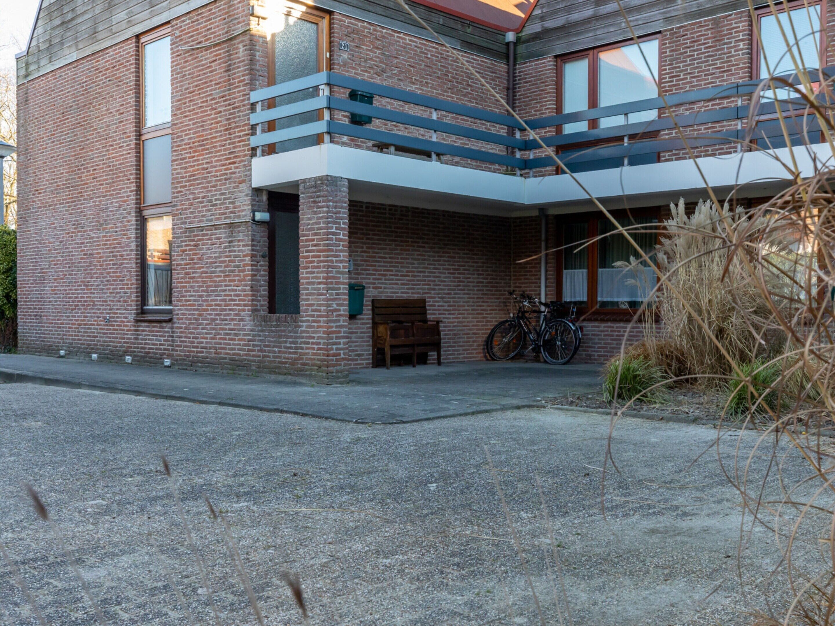 A two-story brick building with a balcony, a bicycle parked outside, and a bench.