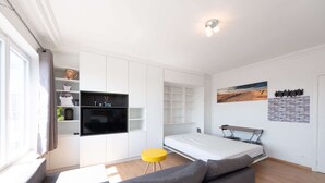 A modern, minimalist room with a sofa, a bed, a TV, and a small table. - Cozy Studio With Terrace and Stunning View (Middelkerke)