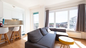 A modern living room with a grey sofa, wooden flooring, and a yellow side table. - Cozy Studio With Terrace and Stunning View (Middelkerke)