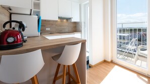A modern kitchen with a kettle, bar stools, and a large window overlooking a parking area. - Cozy Studio With Terrace and Stunning View (Middelkerke)