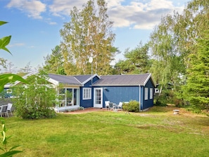 A single-story blue house with a porch, surrounded by a grassy yard and trees. - 4 Star Holiday Home in Nexo (Nexø)