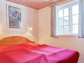 Un dormitorio con una cama de madera, una ventana con cortinas y una lámpara fijada en la pared.