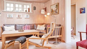 Un cuarto acogedor con piso de madera, un sofá, una mesa de comedor y una silla. Hay cuadros enmarcados en la pared y una lámpara sobre la mesa.