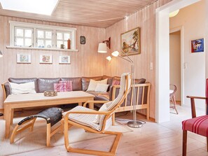 A cozy room with a wooden floor, a sofa, a dining table, and a chair. There are framed pictures on the wall and a lamp on the table. - 4 Star Holiday Home in Nexo (Nexø)