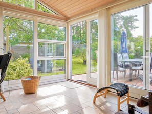Une véranda avec de grandes portes vitrées, un fauteuil en osier, une petite table et un banc.