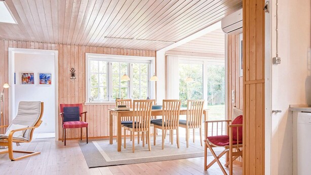 Una habitación acogedora con pisos de madera, una mesa de comedor con sillas, una silla roja, un sillón mecedor de madera y un ventanal grande.