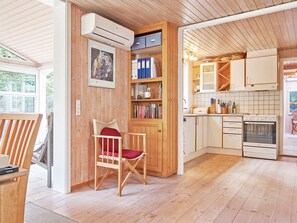 L’intérieur chaleureux d’un chalet en bois comprend un coin repas avec une chaise, une cuisine équipée de placards et d’une cuisinière, ainsi qu’une bibliothèque.
